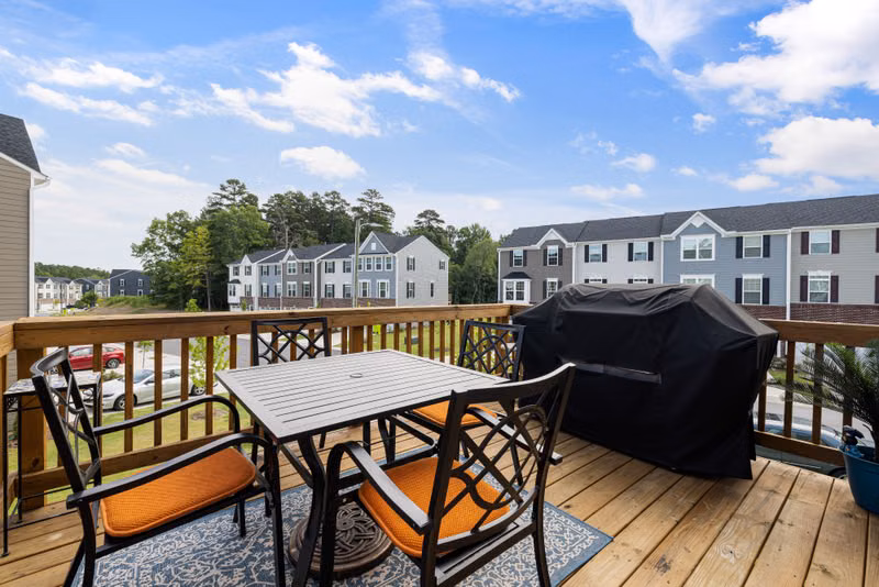 Charming wooden deck with furniture, grill, and suburban view.